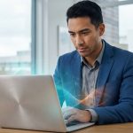 Homme professionnel concentré sur un ordinateur portable avec des effets numériques. Il est dans un bureau lumineux avec fenêtre et plantes.